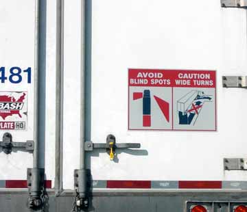 A picture of a sign on the back of a semi truck warning others to be cautious of the truck due to wide turns and blind spots.