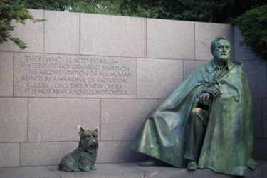 The statue of FDR next to his dog, who sits underneath one of his famous quotes that is inscribed in the stone wall behind it.