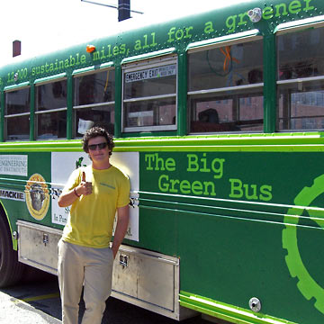 Student standing next to Big Green Bus giving thumbs up sign