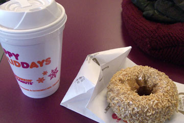 Cup of coffee and toasted coconut donut on table at Dunkin Donut
