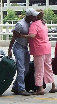 Man with suitcase hugging older woman