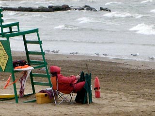 LIfeguard bundled in red parka sitting on beach